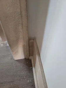Raw wood baseboard installed at a wall corner, debris on subfloor, ready for paint or stain.