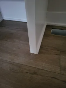 Painted white baseboard corner meeting dark hardwood flooring near a floor vent.