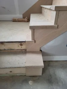 Unfinished wood stair treads with a mitered step end return at the bottom of the staircase