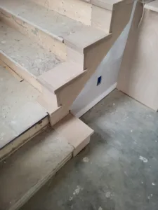 Unfinished wood stair treads turning along the staircase, with a painted wall and a low boxed step below