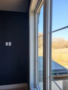 White painted window casing on a tall window in a dark blue accent wall, framing a view of open fields.