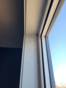 White painted frame between two glass panes with blue sky visible through both, close angled view.