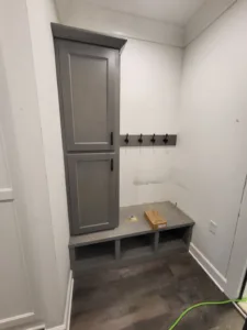 Painted mudroom locker cabinet with bench seating, open cubbies, and wall mounted coat hooks.