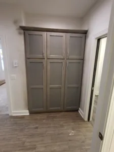 Stained wood three door built-in cabinet with a top shelf, installed in a closet alcove.