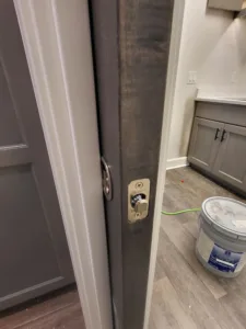 Dark stained pocket door slab with privacy lock mounted on edge, cabinetry visible nearby.