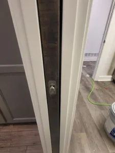 Dark stained pocket door slab edge with flush pull hardware, unfinished, set in a white jamb.