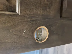 Lockset bore hole in a stained wood door edge with the lock mechanism partly visible inside