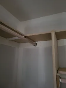 Raw wood hanging rod mounted on cleats in closet corner, particle board shelf visible, unfinished.
