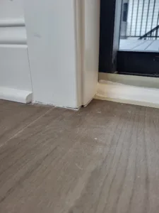 Painted white baseboard installed along vinyl plank flooring next to a door jamb