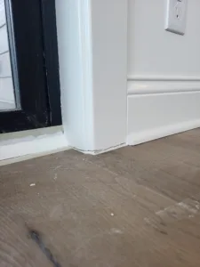 Painted white baseboard meets floor line near a dark framed opening, clean edge detail.