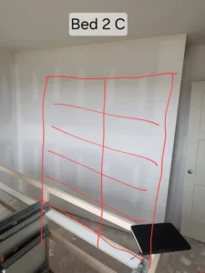 Bedroom wall marked with layout tape for planned closet shelving, drywall stage.