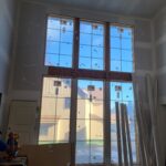 Large multi-pane window wall with dark wood frames and muntins installed in interior space, showing quality glazing and frame installation.