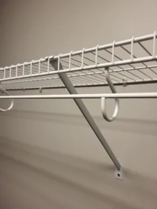 Close-up of white wire shelf with hanging rod, hooks, and wall mount bracket installed in closet.