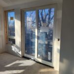 Pre-hung exterior glass doors installed in opening with white jambs and wood exterior trim; drywall and concrete subfloor visible.
