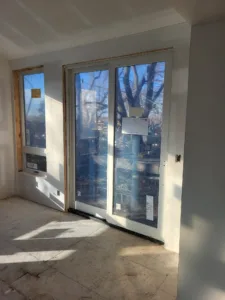 Twin glass patio style doors installed in framed opening with white jambs, drywall stage