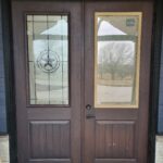 Pair of stained exterior doors with glass and wood panels, installed in black frame with lockset hardware visible.