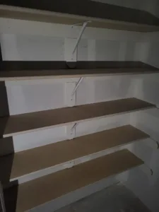 Closet shelving unit with four particle board shelves and white support brackets, unpainted.