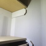 Painted closet shelf with wood hanging rod and metal end cap installed on white wall.