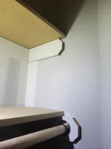 Particle board closet shelf with a wood hanging rod and metal end cap mounted on painted wall.
