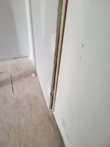Bare inside wall corner meets OSB subfloor, no baseboard installed yet, gap visible at the joint.
