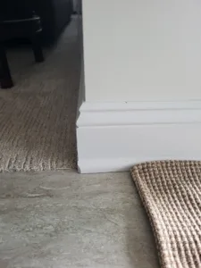 Painted baseboard at floor level meets a carpet to concrete subfloor transition.