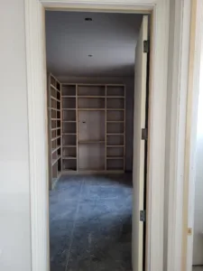 View through doorway into walk-in closet with raw wood shelving lining both walls, unfinished.
