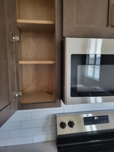 Kitchen cabinet with an open door showing interior shelf and hinge hardware, next to a built-in oven.