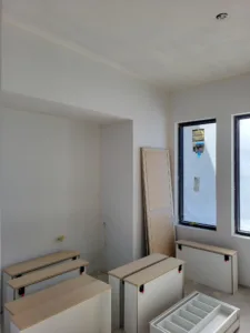 Several raw wood cabinet or bench boxes staged in an empty room near windows, unfinished.