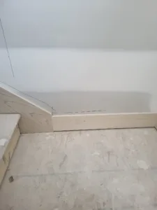 Raw wood trim follows a diagonal stair line at the wall base, unfinished, ready for paint.