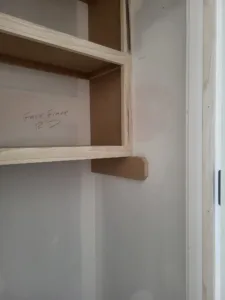 Closet shelving unit with a raw wood face frame and bullnose shelf, unpainted, measurements penciled on wood.