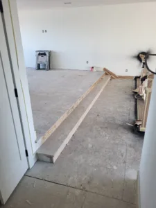 Raw wood baseboard boards staged along a room perimeter during the trim stage, unpainted.