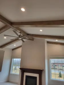 Dark stained wood beams over a stone fireplace with a wood mantel and ceiling fan