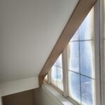 Completed attic room with painted sloped ceiling beam, cased window opening, and finished trim details.