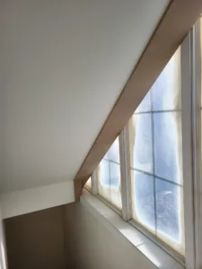 Completed attic room with a painted sloped ceiling and wood trim framing the window.