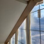 Finished wood handrail mounted to sloped ceiling beside window with paint complete.