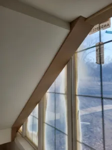 Wood trim beam along a sloped ceiling beside a window, painted white and fully finished.