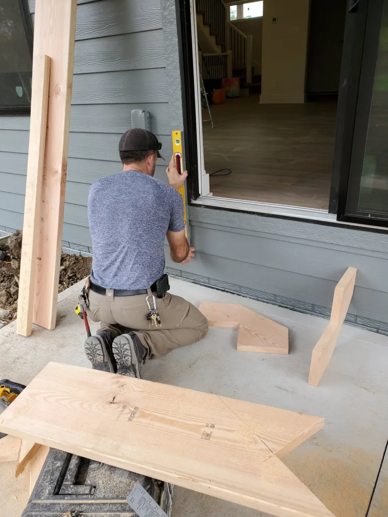 Carpenter holding a level plumb on the house siding by the door, cut stringers on the slab around him