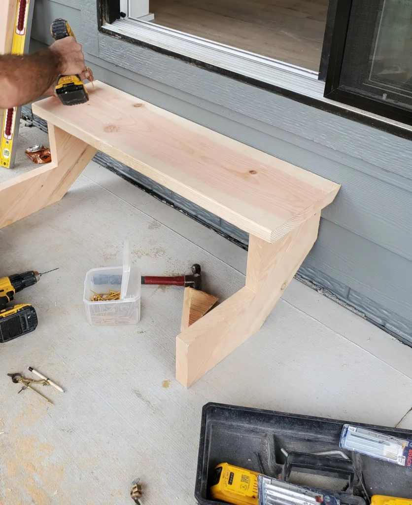 Top tread being screwed down onto both stringers with a cordless drill, screws and tools on the slab