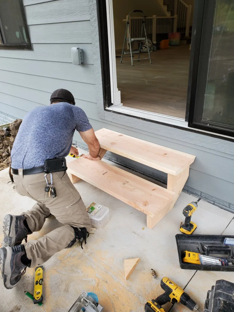 Carpenter fastening the bottom tread, both treads now on the two stringers in front of the patio door