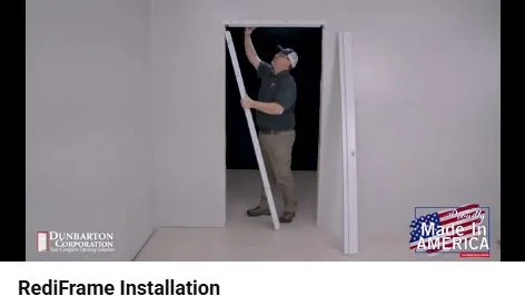 Installer supports the RediFrame head while sleeving the hinge jamb over the finished wall.